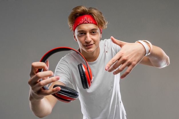 Mec blond mignon tient un casque dans ses mains sur un mur gris