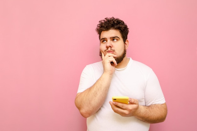 Mec bouclé en t-shirt blanc et barbe réfléchie isolé sur fond rose