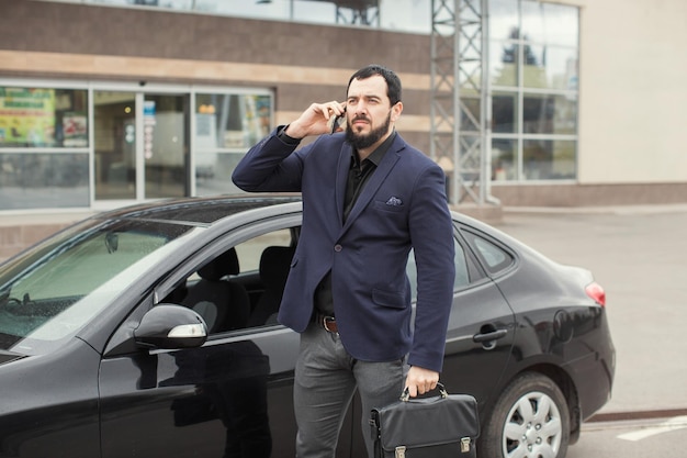 Un mec brune avec une barbe près d'une voiture noire