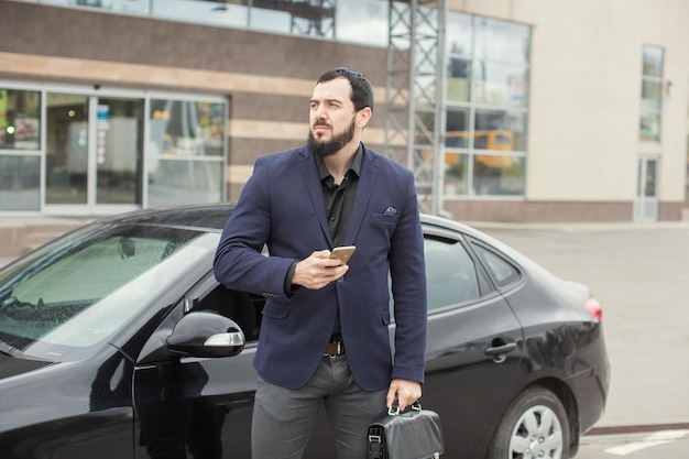 Un mec brune avec une barbe près d'une voiture noire