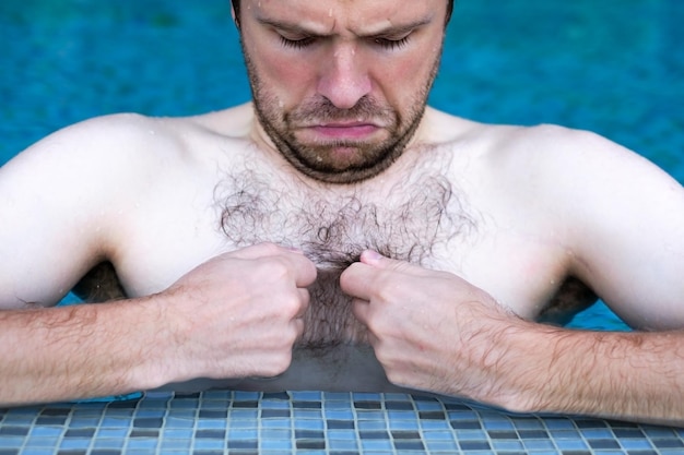 Mec caucasien nageant dans la piscine, il regarde ses cheveux sur la poitrine