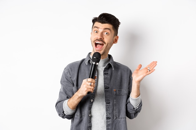 Un mec élégant excité donne un discours, parle au microphone, joue ou chante au karaoké, debout sur fond blanc.