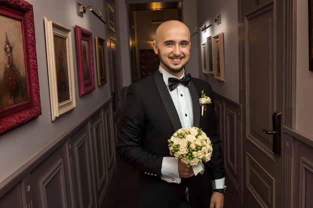 Mec élégant gai dans un smoking avec un bouquet de sourires de roses