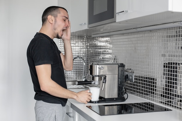 Mec endormi le matin dans la cuisine à préparer du café dans une machine à café.