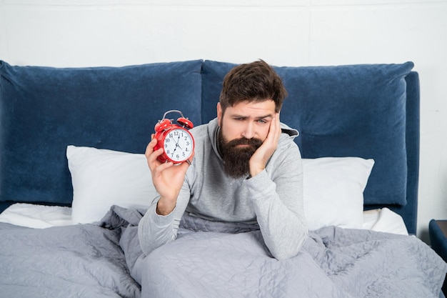 Un mec endormi tenant un réveil étant au lit le matin