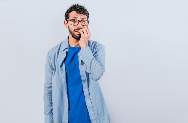 Un mec avec une expression inquiète sur fond isolé Un jeune homme nerveux avec une expression inquiète se mord les ongles et regarde anxieusement le concept d'homme nerveux