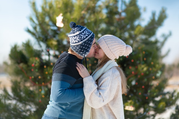 Mec avec une fille embrasse sur un arbre de Noël vert décoré avec des jouets de fête et des guirlandes en hiver dans la forêt. Romance d'hiver