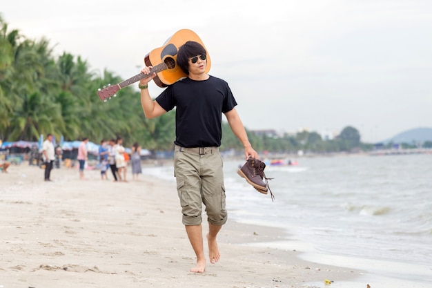 Mec avec guitare debout sur la plage, pantalon cargo