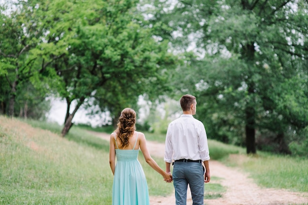 Mec heureux dans une chemise blanche et une femme dans une robe turquoise marchant dans le parc forestier