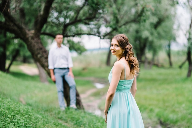 Mec heureux dans une chemise blanche et une femme dans une robe turquoise marchant dans le parc forestier