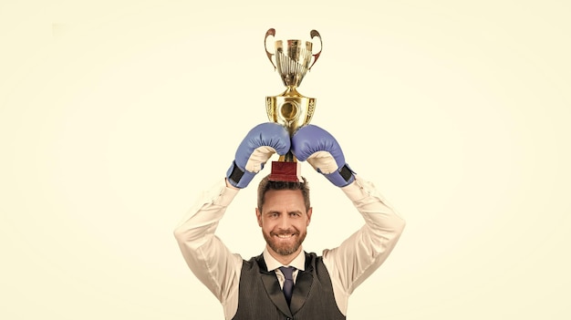 Un mec heureux dans des gants de boxe et des tenues de soirée tient la coupe du champion isolée sur la victoire de fond blanc