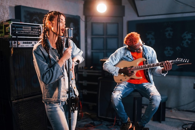 Un mec joue de la guitare, une fille chante Un homme afro-américain avec une fille blanche qui répète ensemble dans le studio