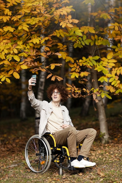 Un mec joyeux une personne handicapée est assise dans un fauteuil roulant et prend un selfie sur un smartphone