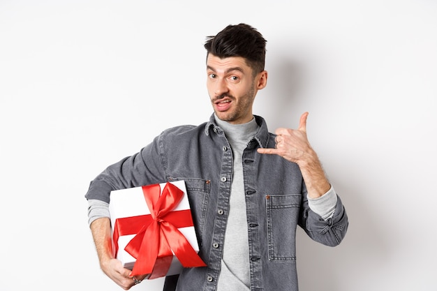 Mec macho avec spectacle de boîte-cadeau appelez-moi geste de téléphone, flirtant avec vous, debout vantard sur blanc. Concept de relation et de la Saint-Valentin.