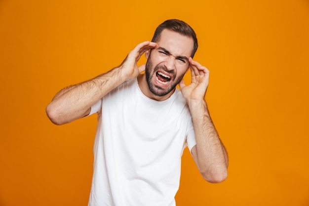 Un mec malade en t-shirt hurlant et se frottant les tempes à cause de maux de tête tandis que, isolé sur jaune