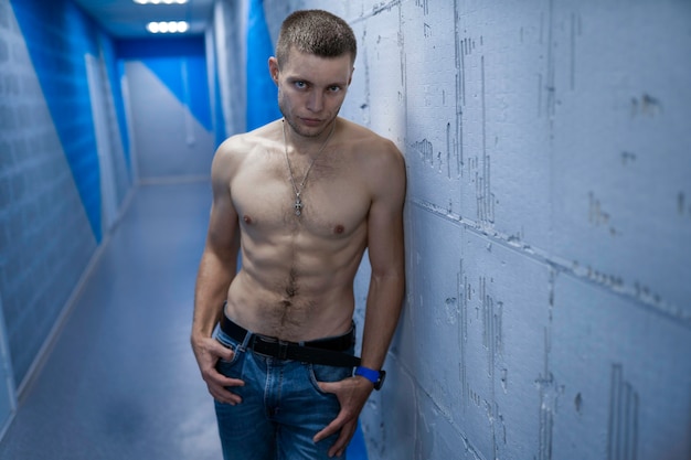 Photo un mec maussade en jeans avec torse musclé nu se tient appuyé son épaule contre le mur