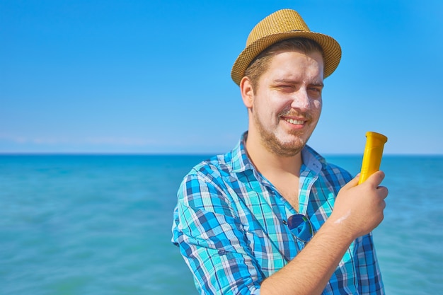 Un mec met une crème solaire sur le visage. Un homme au bord de la mer, le visage couvert de crème solaire.