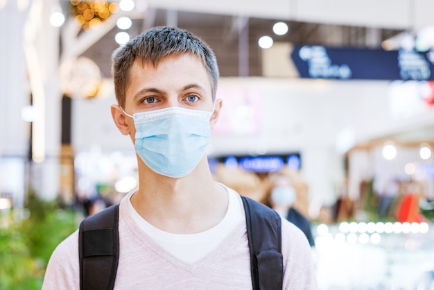 mec mignon dans des vêtements décontractés, dans un masque de protection avec un sac à dos sur le dos dans un centre commercial