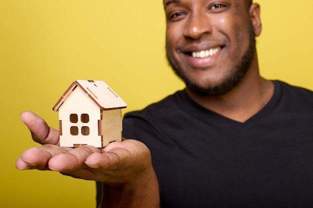 Photo un mec mignon à la peau sombre étend une maison de jouets dans la paume de sa main, symbole de chaleur