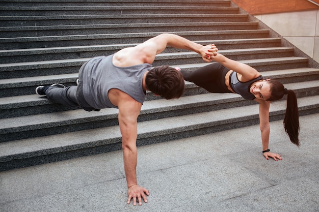 Mec musclé et fille mince est debout dans une position de planche sur les marches