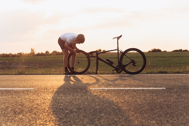 Mec musclé en vêtements de sport et casque de protection, réparation de roue sur vélo à l'extérieur