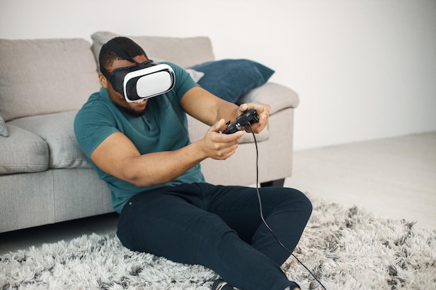 Mec noir avec des lunettes de réalité virtuelle assis sur un tapis dans le salon