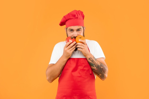 Mec sérieux en tablier de cuisine et toque sentant les tomates fond jaune chef