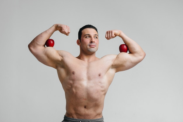 Mec sexy sportif posant sur un fond blanc avec des fruits lumineux. Régime. Régime équilibré