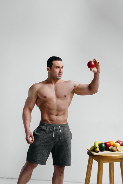 Mec sexy sportif posant sur un fond blanc avec des fruits lumineux. Régime. Régime équilibré.