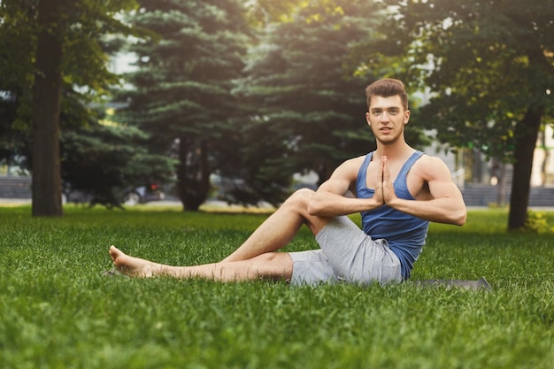 Mec sportif pratiquant le yoga assis sur l'herbe dans le parc. Jeune homme méditant les yeux fermés, namaste sur l'herbe verte dans le parc, espace pour copie