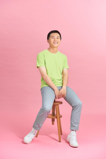 Mec en t-shirt assis sur une chaise devant un mur rose, look d'homme