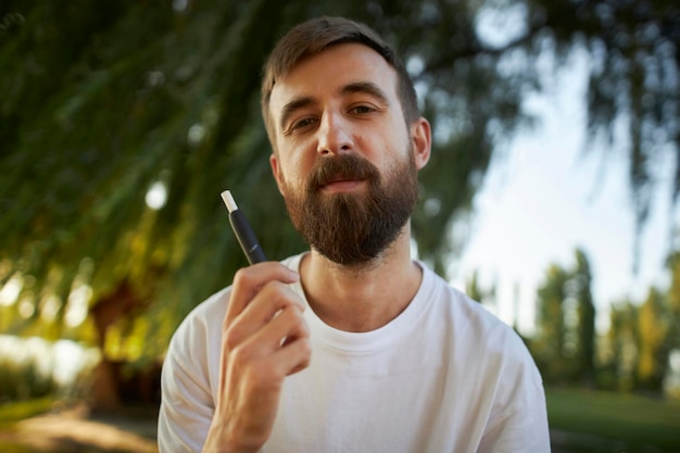 mec en t-shirt blanc avec une cigarette électronique dans le parc. Le gars est titulaire d'un électronique