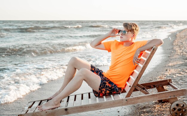 Un mec en t-shirt et short est assis sur une chaise longue au bord de la mer