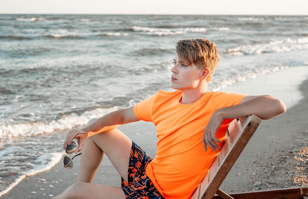 Un mec en t-shirt et short est assis sur une chaise longue au bord de la mer