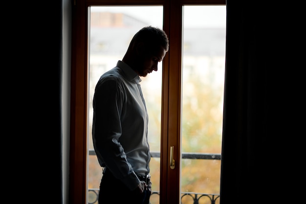 Mec triste dans une chemise blanche avec une courte presy debout à la fenêtre. photo de haute qualité