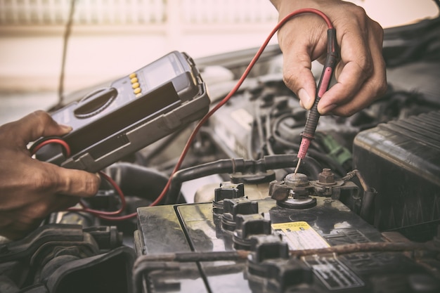 Mécanicien automobile à l'aide de l'outil d'équipement de mesure pour réparer la batterie de voiture.