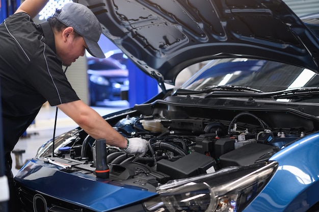 Un mécanicien automobile asiatique examine un problème de panne de moteur devant une automobile