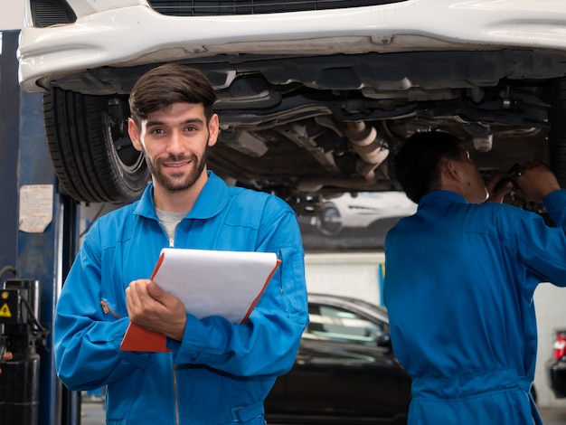 Mécanicien automobile caucasien en uniforme tenant le presse-papiers de l'ordre de service travaillant dans le garage. liste de contrôle du technicien pour réparer une voiture dans le garage.