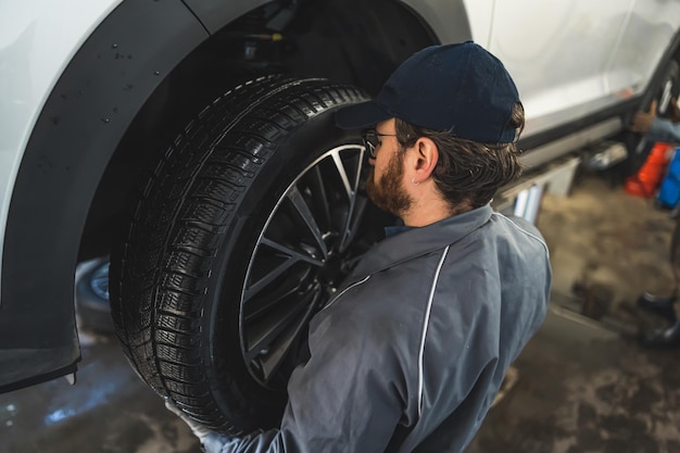 Mécanicien automobile changeant les roues d'une voiture blanche levée dans une station-service de réparation