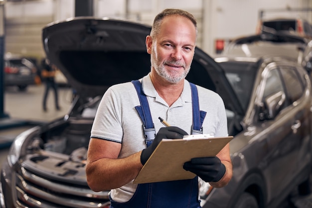 Mécanicien automobile écrit sur le presse-papiers à la station-service