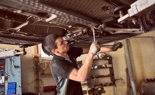 Mécanicien automobile faisant des efforts pour foutre le détail de l'automobile Vérification et entretien de la voiture dans le garage de l'atelier Service automobile