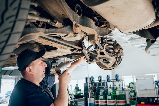 Mécanicien automobile inspectant la roue et la suspension des détails de l'automobile levée à la station-service de réparation