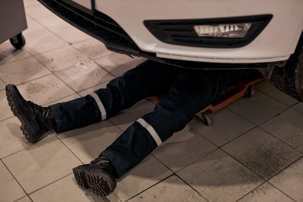 Photo mécanicien automobile mâle travaillant seul sur le plancher de réparation bas de voiture regarder les détails dépanner le c