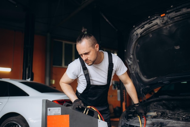 Mécanicien automobile masculin remplissant le climatiseur de la voiture et vérifiant le système d'huile du compresseur causé par le climatisateur de la voiture n'est pas froid