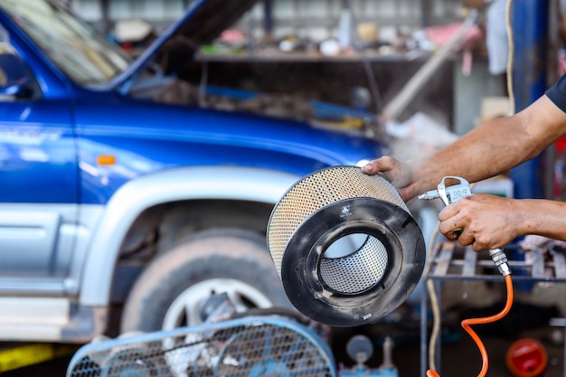 Le mécanicien automobile nettoie et souffle le filtre à air de la voiture dans la station de réparation automobile.