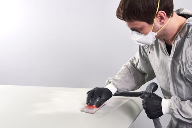 Mécanicien automobile portant un masque facial polissant et polissant le capot de voiture dans un atelier de réparation automobile