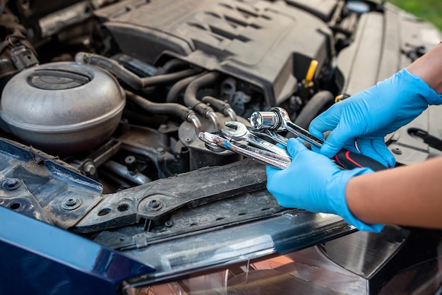 Un mécanicien automobile ou un réparateur répare un moteur de voiture à la main dans un atelier automobile avec une clé