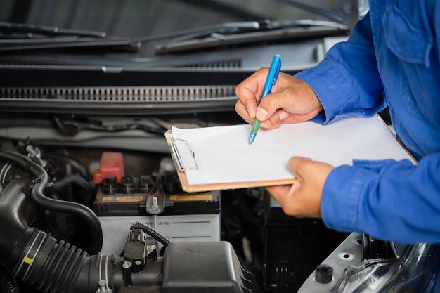 Mécanicien automobile tenant la liste de contrôle du presse-papiers la voiture à l'atelier de mécanique