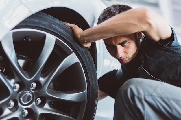 Photo mécanicien automobile travaillant en atelier vérifiant le pneu sur la roue station-service