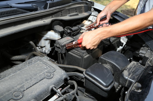 Un mécanicien automobile utilise des câbles de démarrage de batterie pour charger une batterie déchargée